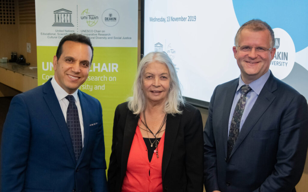 Audience listening to Professor Marcia Langton standing with Professor Fethi Mansouri and the VC at the UNESCO Oration 2019