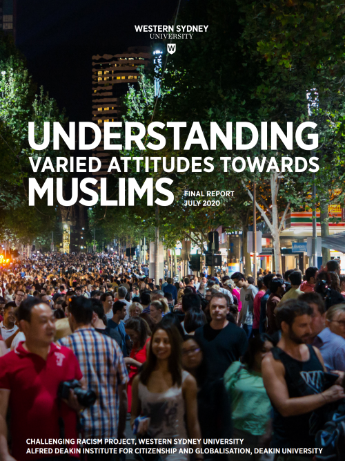 A woman wearing a peach coloured hijab and a lighter pink top, sitting on the sand at the beach in bright daylight. We see her from the back, facing the waves.