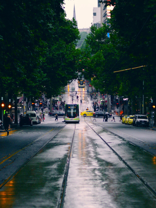 A woman wearing a peach coloured hijab and a lighter pink top, sitting on the sand at the beach in bright daylight. We see her from the back, facing the waves.