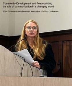 A woman with long hair and glasses speaking at a podium