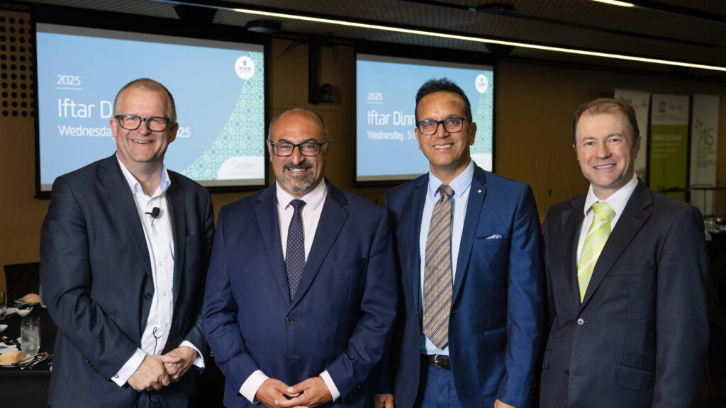 Four men in suits standing together smiling for the camera after presenting the Iftar dinner 2025.