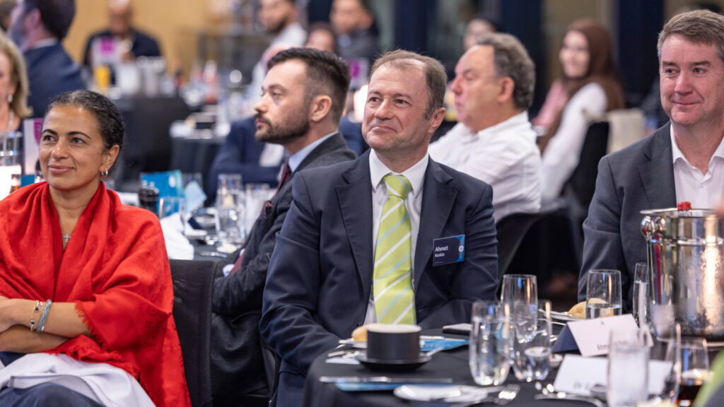 Attendees seated around a table, listening to a speaker at the Iftar dinner 2025.