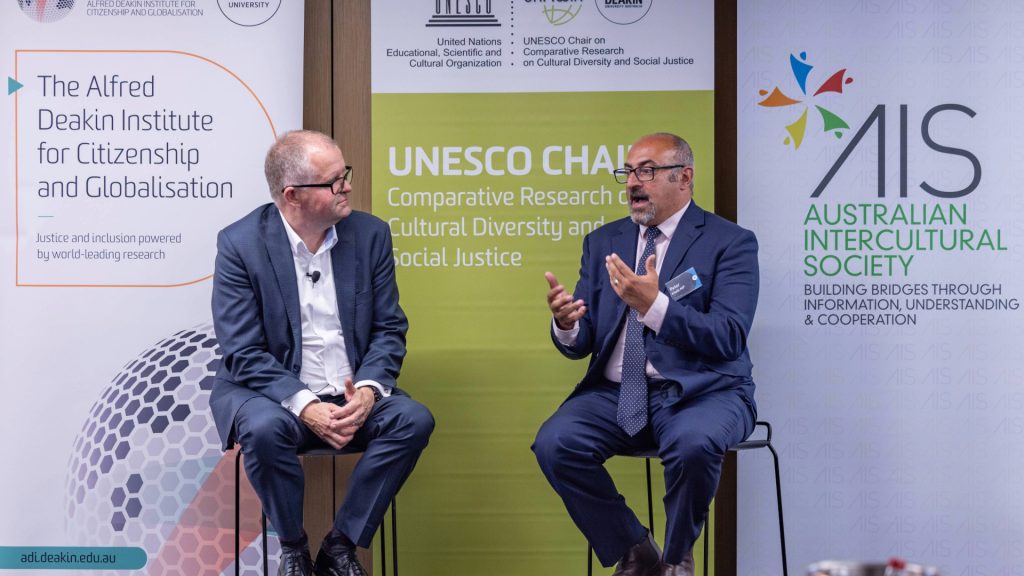 Two men in suits on stage having a discussion at the 2025 Iftar.