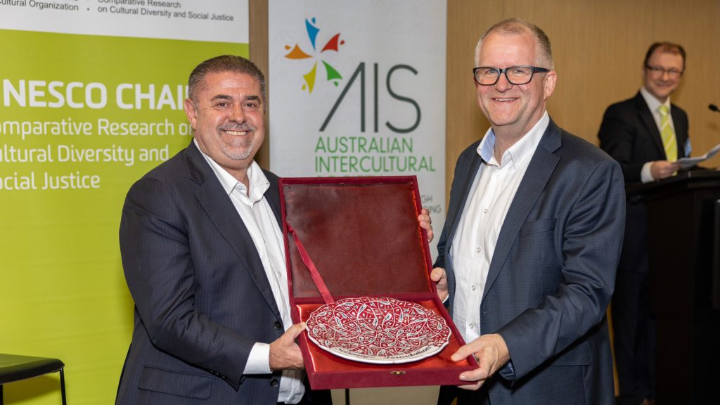 Two men holding a large decorative plate between them.
