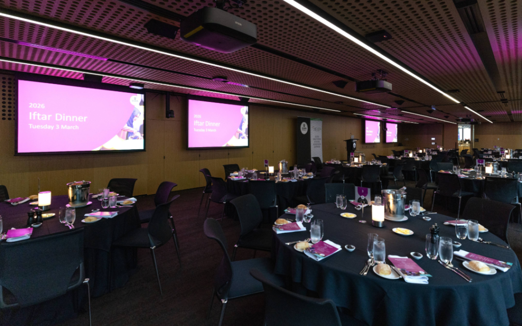 A large room of carefully set round tables, with low lighting, empty of people before the event.